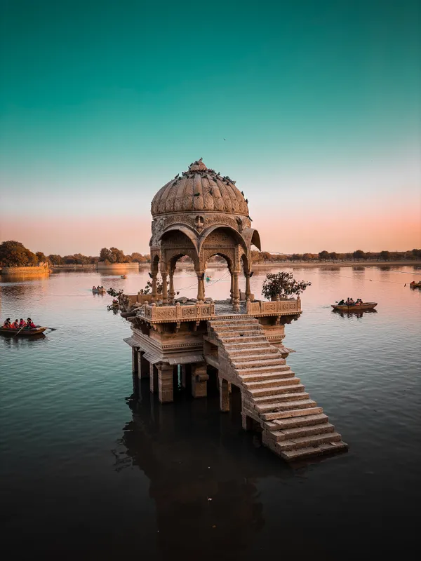 Stone chhatri with steps into Gadisar Lake at dusk, boats on the water